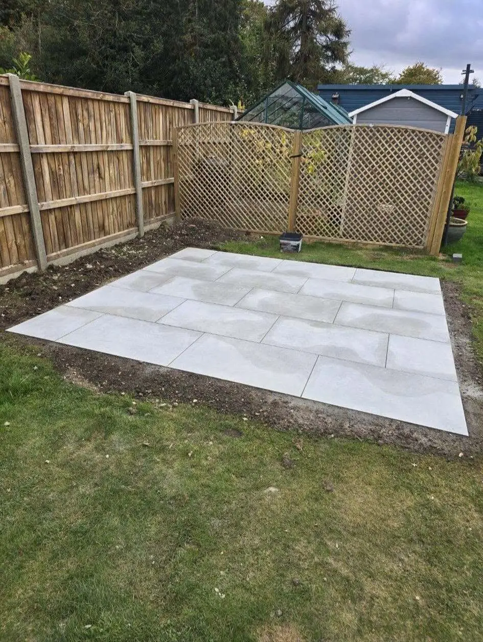 Light grey porcelain patio laid in a garden beside a closeboard fence and trellis